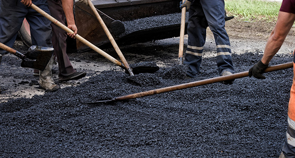 workers using shovels to spread asphalt on a road during a paving project showcasing teamwork in construction and the importance of quality materials in seven steps