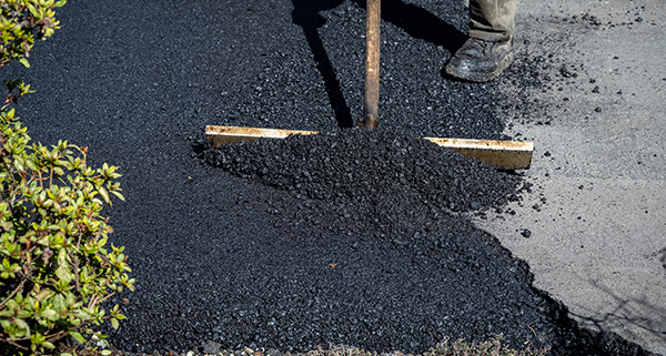 person using a shovel to spread fresh asphalt on a surface surrounded by green shrubs asphalt installation 3 steps process